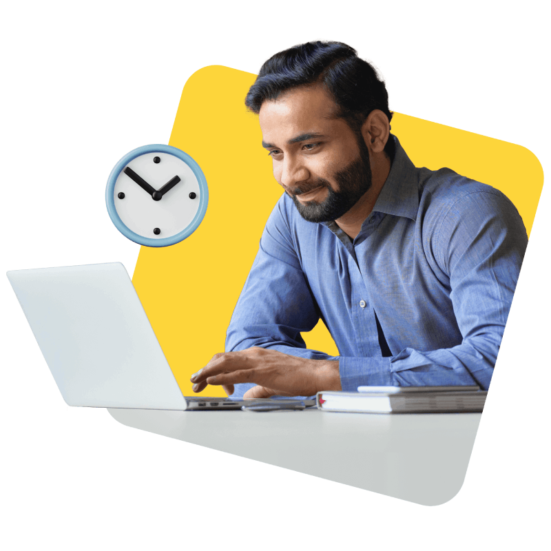 A man seated at a desk, focused on his laptop, with a clock visible in the background indicating the time.