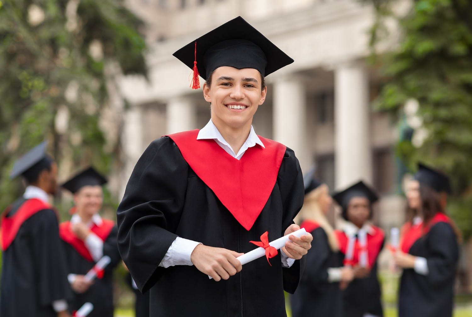 A young man proudly wearing a graduation gown, holding his diploma with a smile on his face.